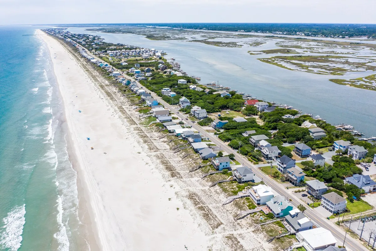 A tranquil view featuring beachfront properties lining the shore, calm waters, a wide stretch of sandy beach, and lush coastal vegetation. The image conveys the relaxed mood of enjoying the shoreline, engaging in water activities, and connecting with the island’s natural side.