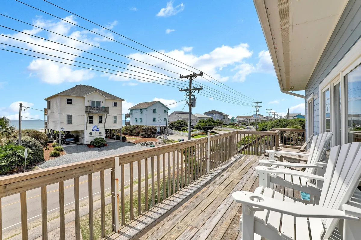 The image showcases the exterior of the beachfront house, with inviting deck chairs overlooking sweeping ocean views. Surrounding coastal homes provide a classic beach neighborhood atmosphere, and the spacious deck promises moments of relaxation.
