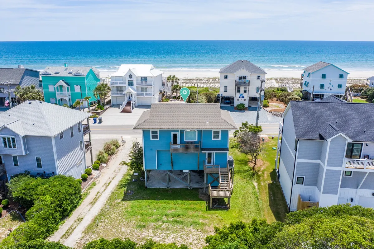 A serene exterior view of a beachfront house with a green lawn, overlooking the vast Atlantic Ocean. The image shows the inviting setting for family gatherings with ample space for outdoor activities. Surrounding houses and the open sky add to the sense of community and relaxation.