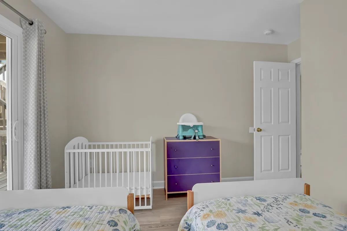 A cozy bedroom setup with a crib (baby cradle), purple dresser, and twin beds. The layout feels nurturing and welcoming, tailored for families with young children.
