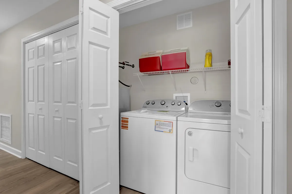 A tidy laundry area featuring a washing machine, dryer, shelving unit, and storage bins. The space is organized and practical, emphasizing convenience for guests managing their needs during their stay.