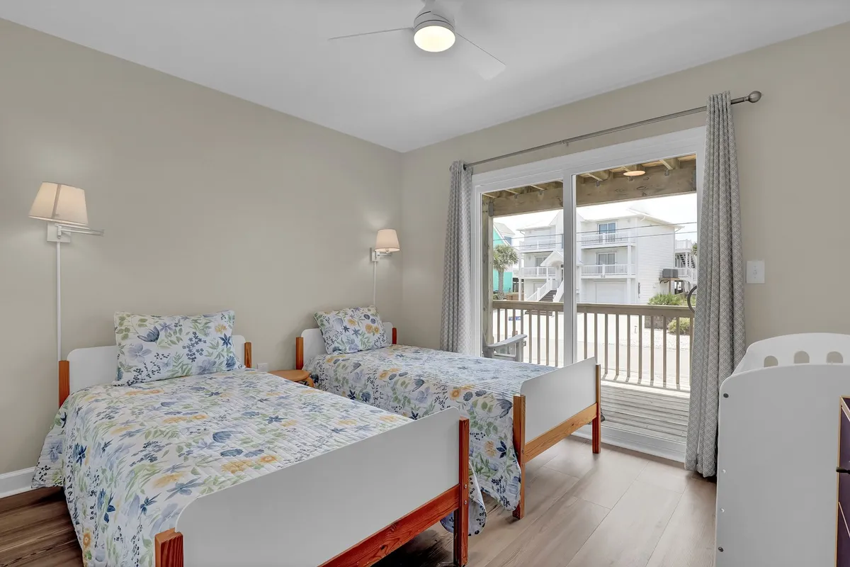 This image features two twin beds with floral bedding, a large glass sliding door that opens to a balcony, and wall-mounted lamps. The abundance of natural light and the possibility of stepping onto the balcony evoke a sense of calm and connection to the outdoors.