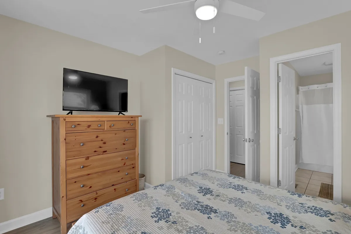A bedroom with a large bed featuring patterned bedding, a wooden dresser with a TV, and doors leading to other rooms. The space is inviting and designed for relaxation after a day in the sun.
