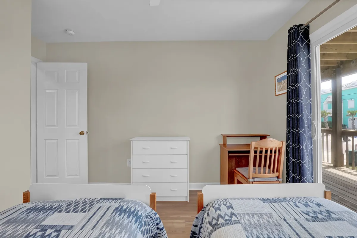 A tranquil bedroom with two twin beds, a dresser, desk, chair, and window with curtains. The cozy setting is ideal for relaxation, reading, and winding down after a day of travel or activity.
